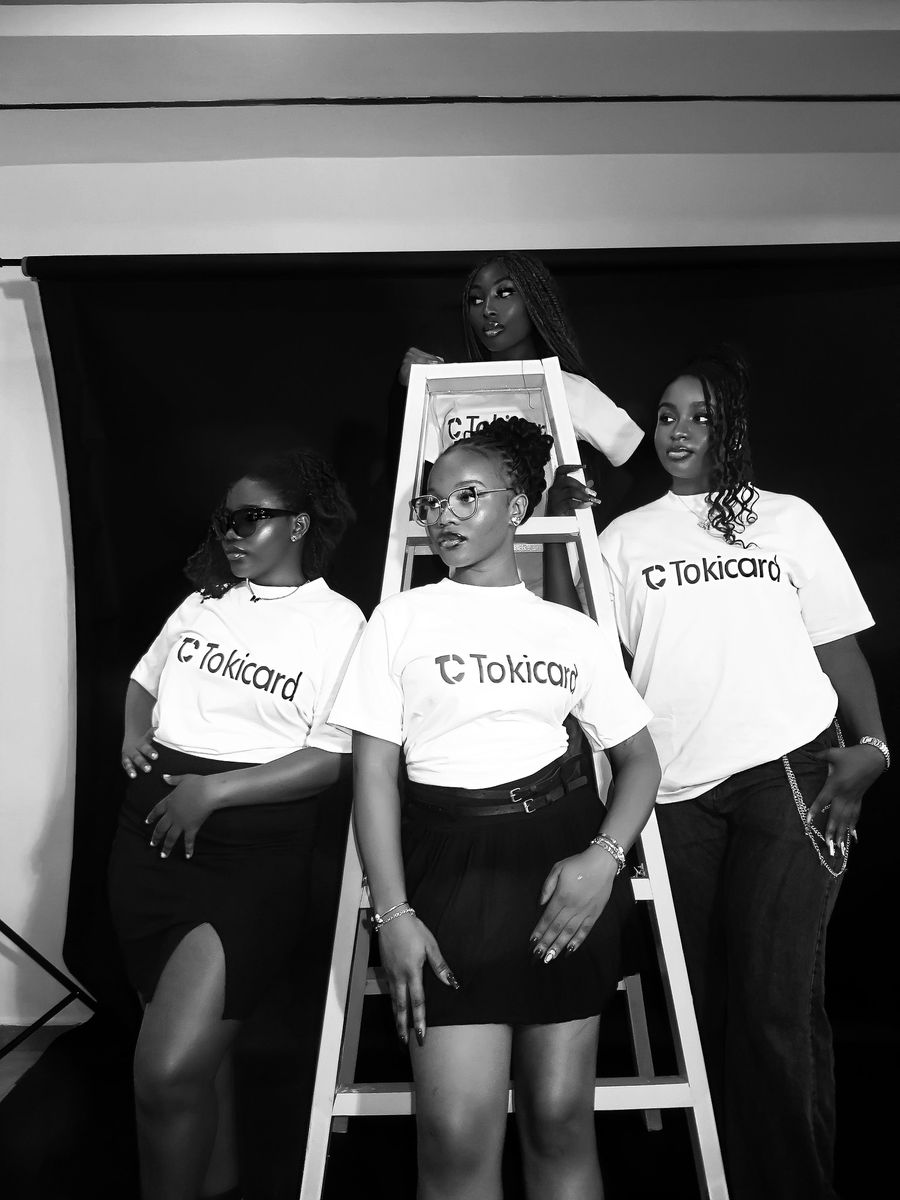 Three women in TokiCard shirts posing by a ladder